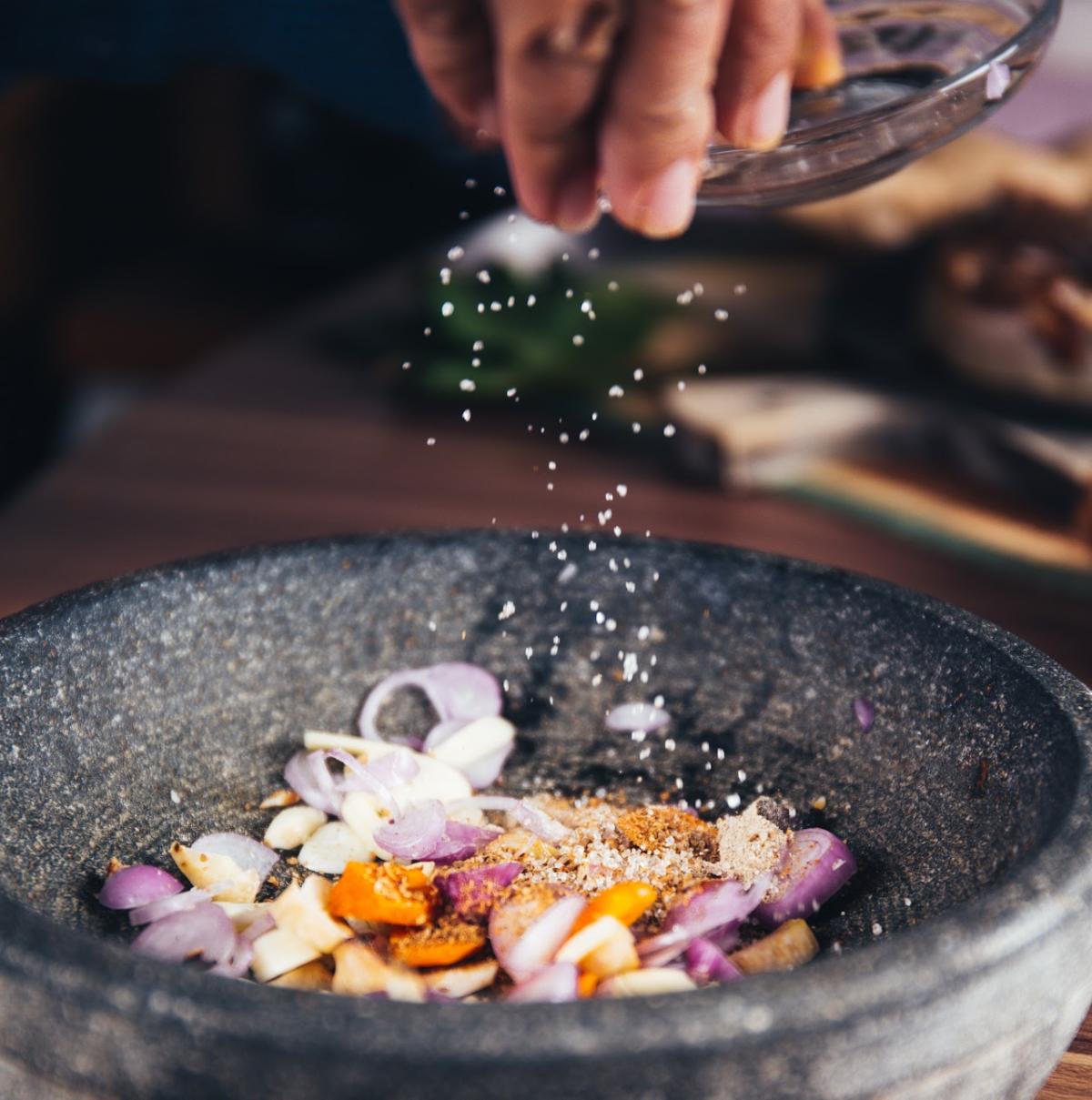 A cook sprinkles salt on an Asian salad.